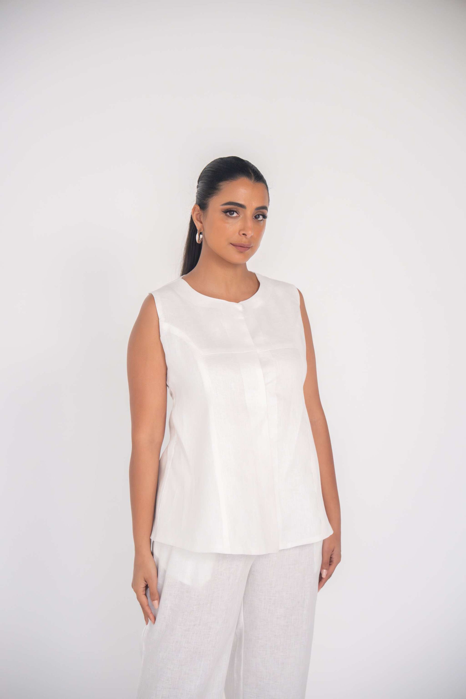 Minimalist white sleeveless linen blouse with round neckline and front seam detailing for a lightweight summer look
