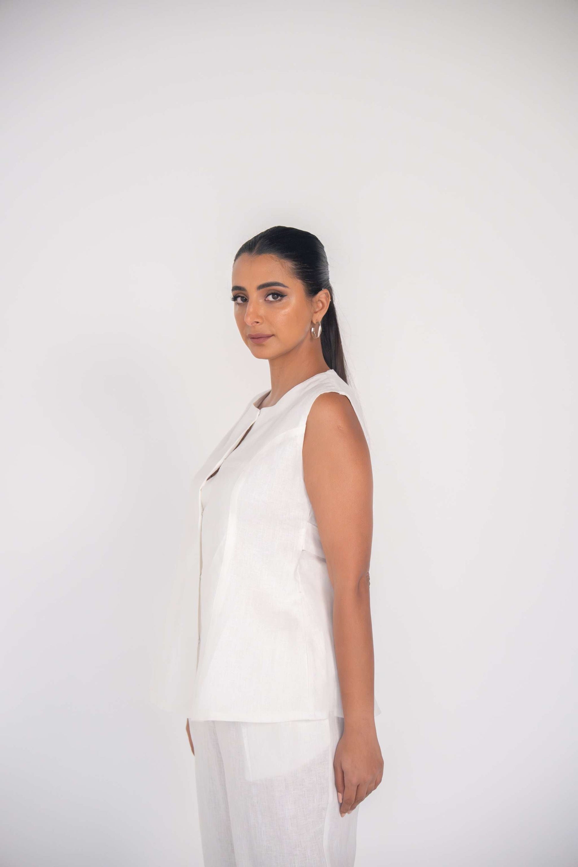 Woman wearing sleeveless white linen blouse with round neckline and subtle front seam detailing.
