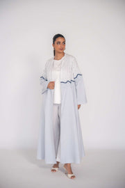 woman wearing a soft blue refined linen abaya with hand-applied white and navy beadwork in a wave pattern across the bodice and sleeves