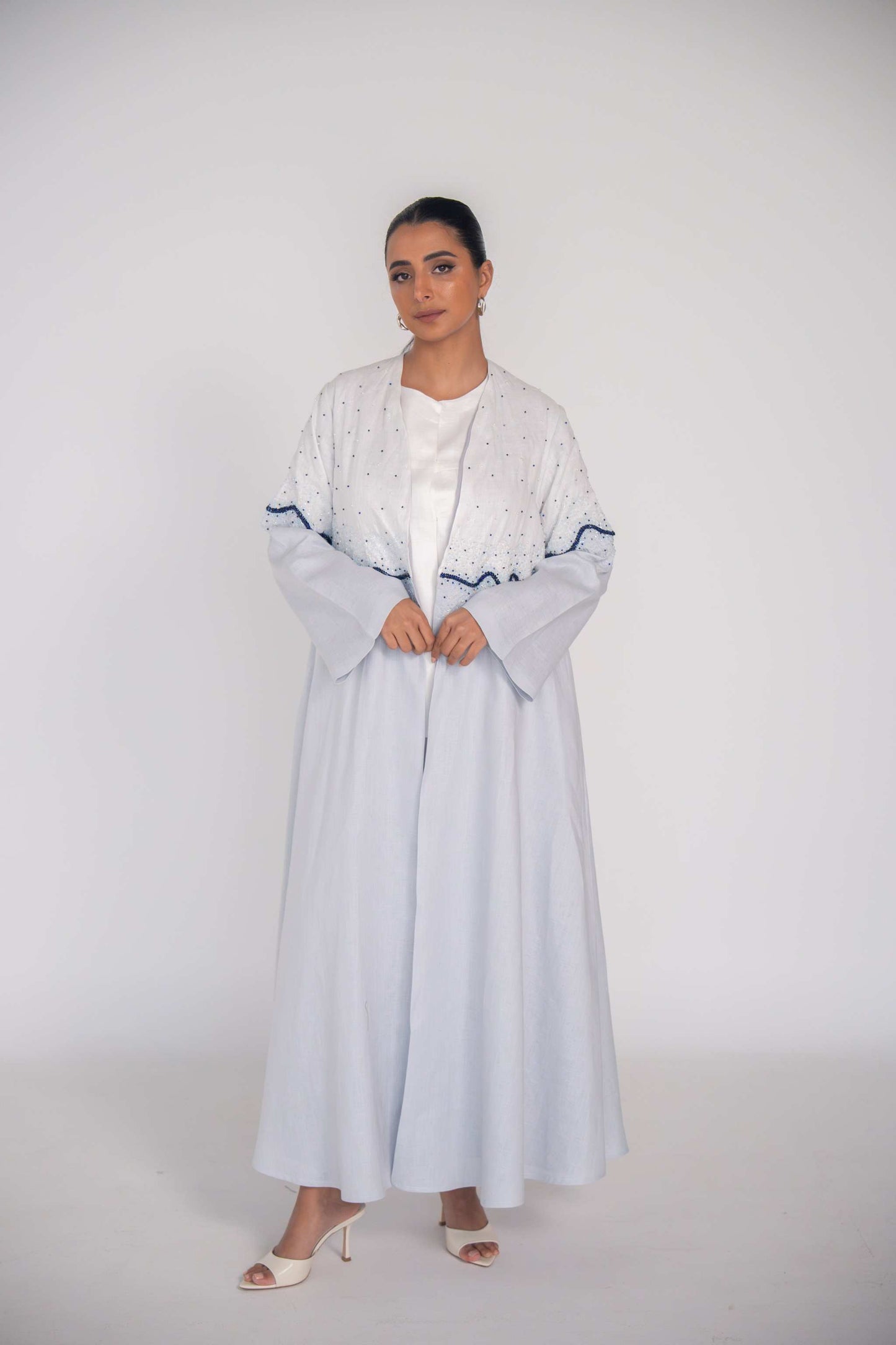 Light blue linen abaya with hand-applied white and navy beadwork in wave gradient, chiffon lining, and flowing cut for elegant warm-weather wear
