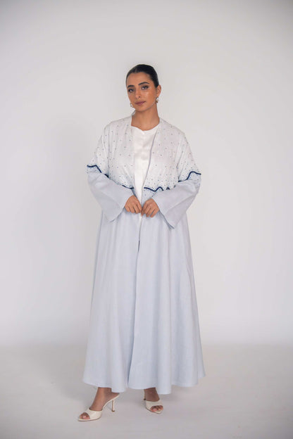 Light blue linen abaya with hand-applied white and navy beadwork in wave gradient, chiffon lining, and flowing cut for elegant warm-weather wear