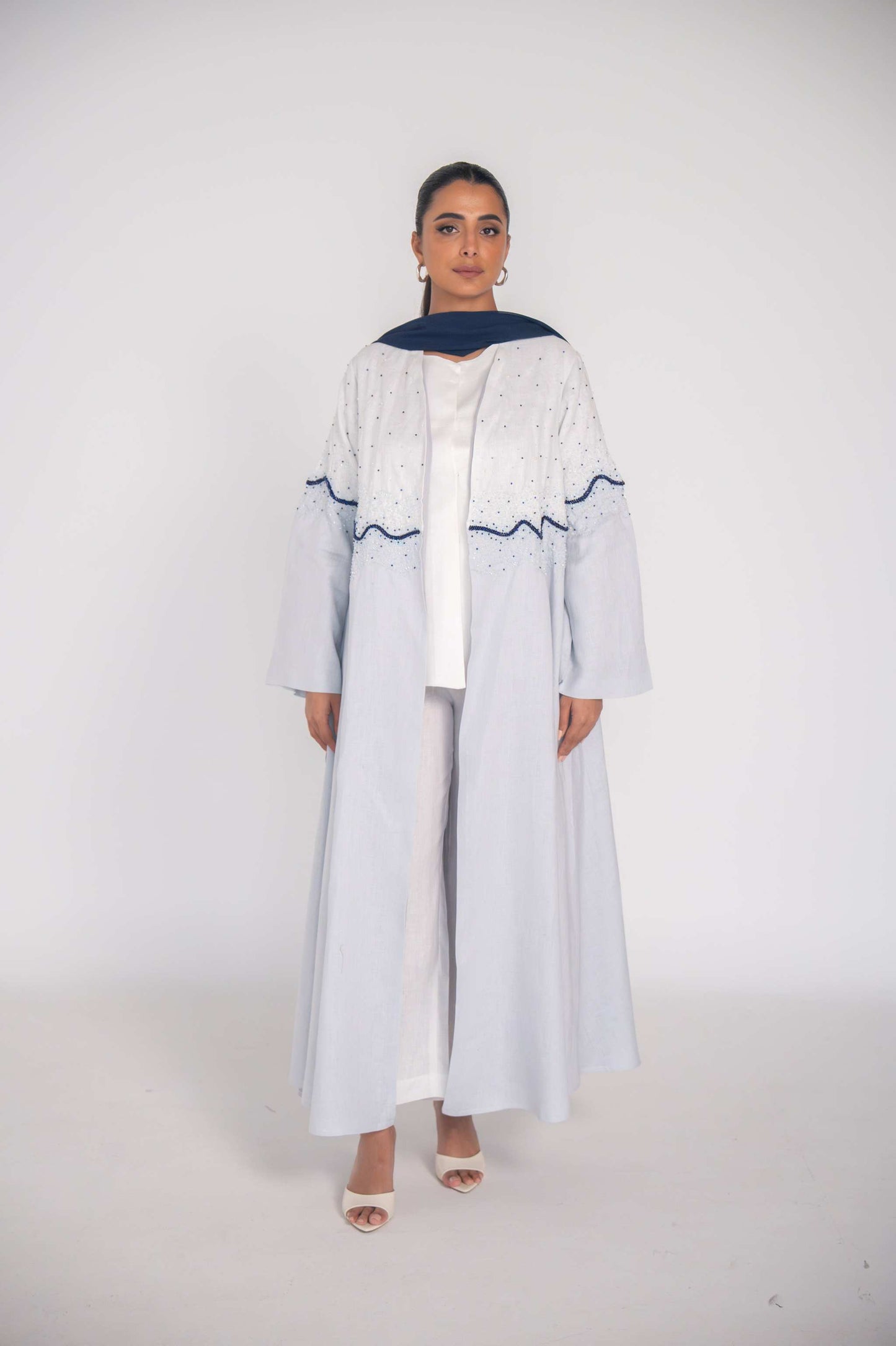 Elegant linen abaya with hand-applied white and navy beadwork in wave gradient, chiffon lining, and flowing cut for warm-weather wear