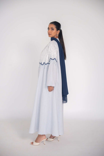 Woman wearing a white linen abaya with navy wave beadwork and chiffon lining, styled for warm weather.