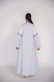 Back view of a light linen abaya with hand-applied white and navy beadwork on sleeves and bodice, featuring a flowing cut and chiffon lining for comfort.