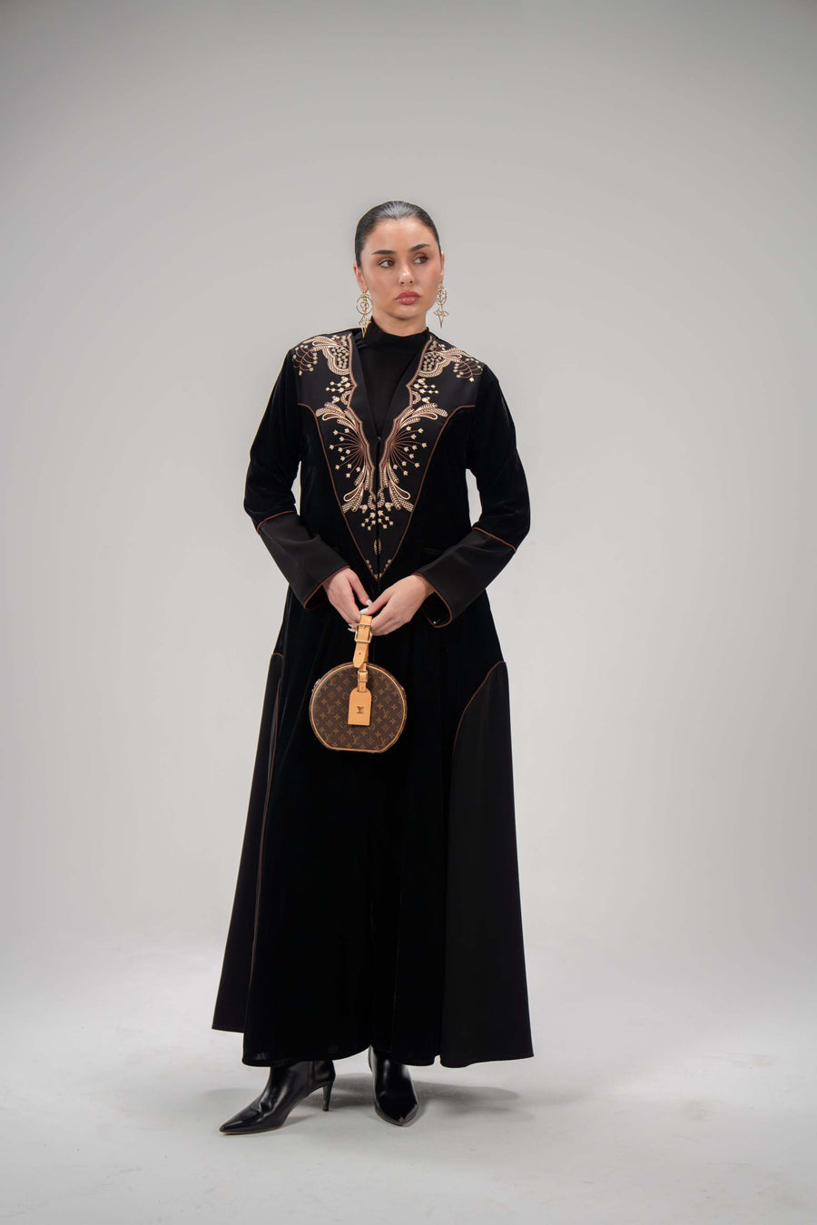 woman wearing black abaya plush velvet with gold machine embroidery holding round handbag