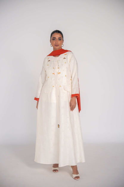Elegant white abaya in textured jacquard fabric with hand-embroidered sunbursts and orange slice motifs, lined with vibrant orange chiffon and featuring rounded neckline and flap pockets.