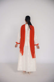 Woman wearing a white abaya made of textured jacquard fabric with an orange chiffon scarf draped over her shoulders, shown from the back.