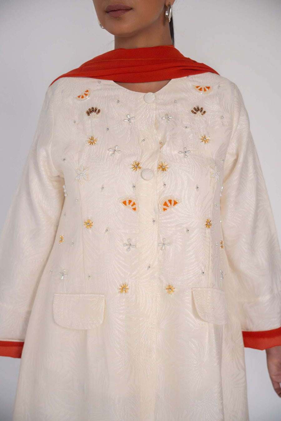 Elegant abaya in textured jacquard fabric with hand-embroidered sunbursts and orange slice motifs, accented with tonal buttons and flap pockets.