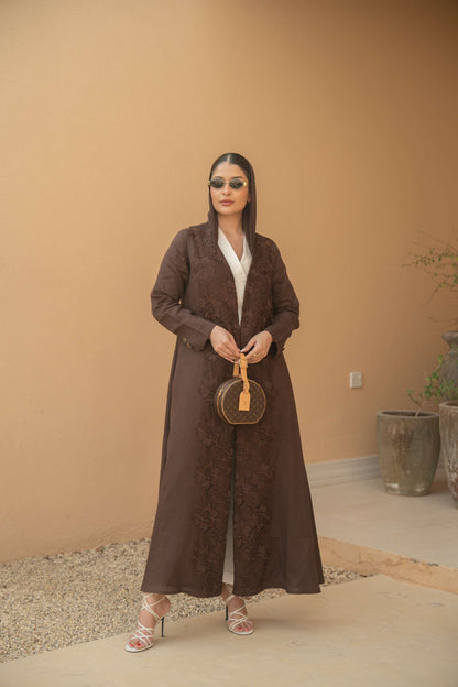 Woman wearing deep mocha brown Mocha Bloom Abaya with floral embroidery and open front style standing outdoors