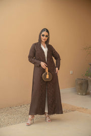 Woman wearing a deep mocha brown Mocha Bloom Abaya with floral embroidery, open front, lightweight fabric, styled with sunglasses and white heels, holding a round handbag.