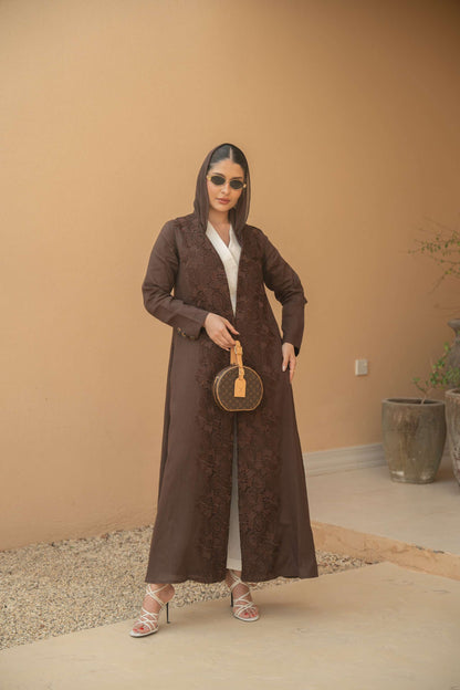 Woman wearing a deep mocha brown Mocha Bloom Abaya with floral embroidery, open front, lightweight fabric, styled with sunglasses and white heels, holding a round handbag.