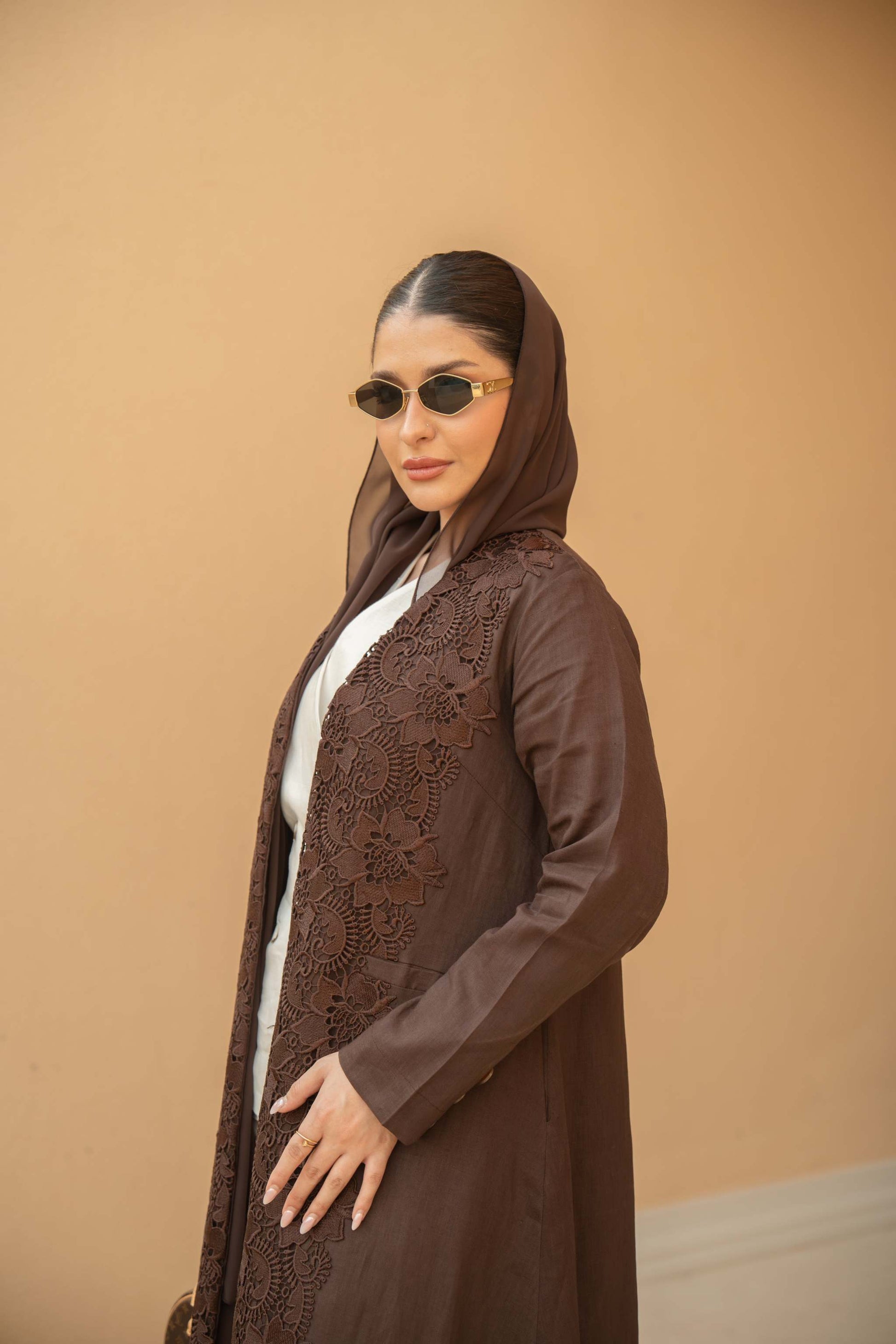 Woman wearing a deep mocha brown Mocha Bloom Abaya with floral lace embroidery and sunglasses