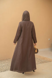 Back view of a woman wearing a deep mocha brown Mocha Bloom Abaya with a flowing lightweight fabric and long sleeves, paired with a matching headscarf and holding a woven handbag.