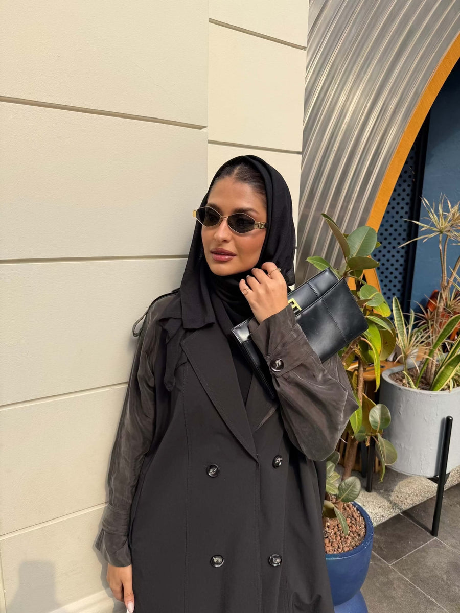 Woman wearing a black trench coat with unique sleeved design and sunglasses holding a black clutch bag - trench coat and sleeves