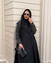 Woman wearing a black trench coat with unique sleeved design and sunglasses holding a black clutch bag - trench coat and sleeves