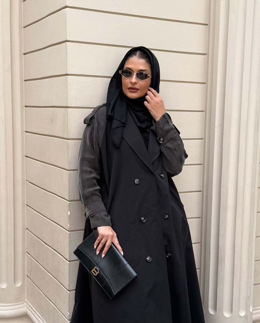 Woman wearing a black trench coat with unique sleeved design and sunglasses holding a black clutch bag - trench coat and sleeves