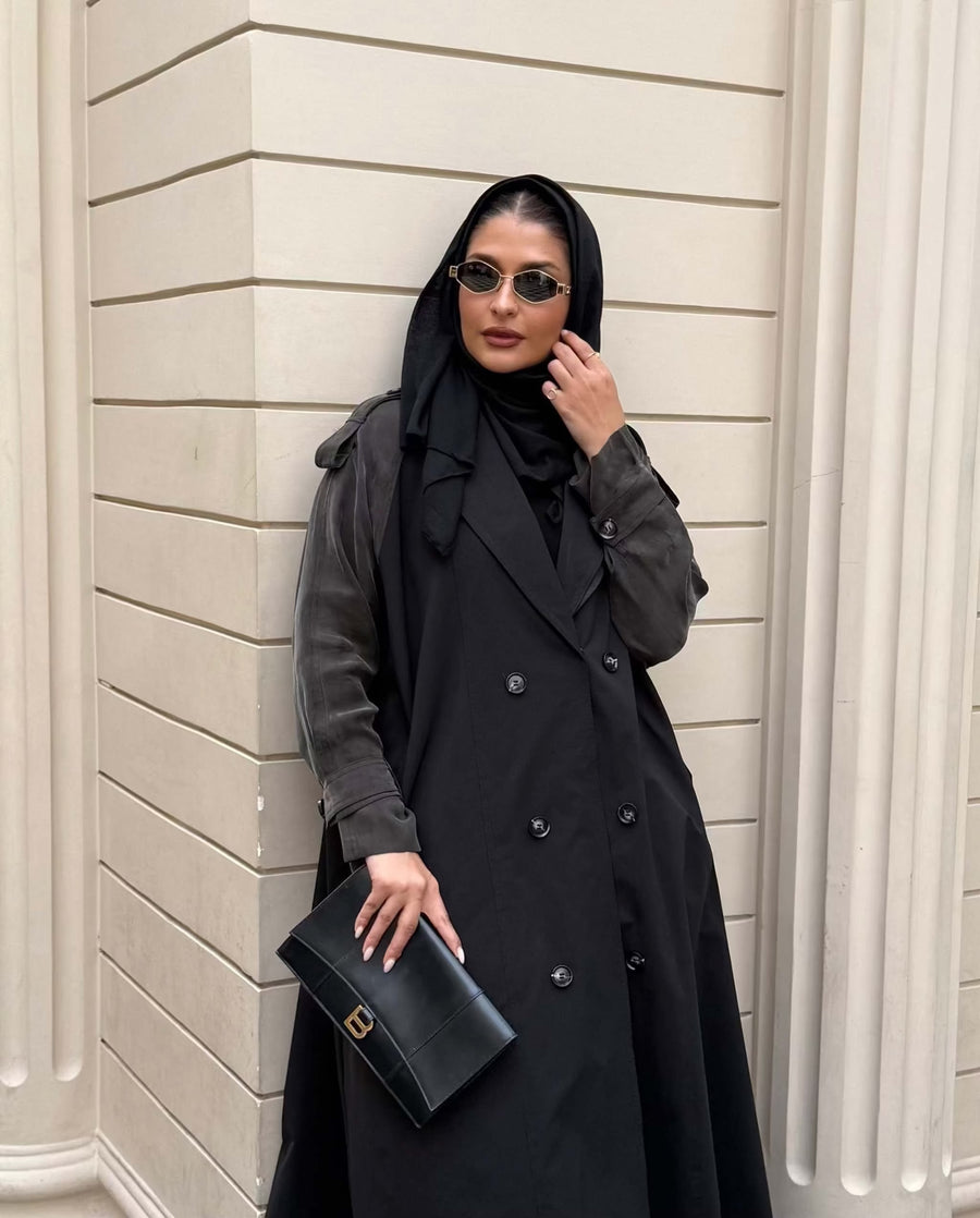 Woman wearing a black trench coat with unique sleeved design and sunglasses holding a black clutch bag - trench coat and sleeves