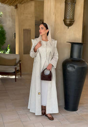 woman wearing a beige linen abaya with trench-style silhouette and matching sheila holding a brown handbag - beige abaya