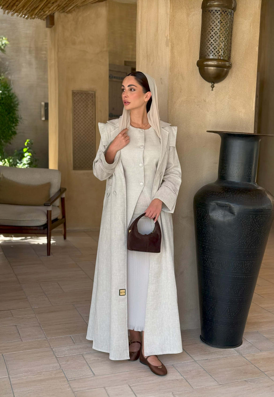 woman wearing a beige linen abaya with trench-style silhouette and matching sheila holding a brown handbag - beige abaya