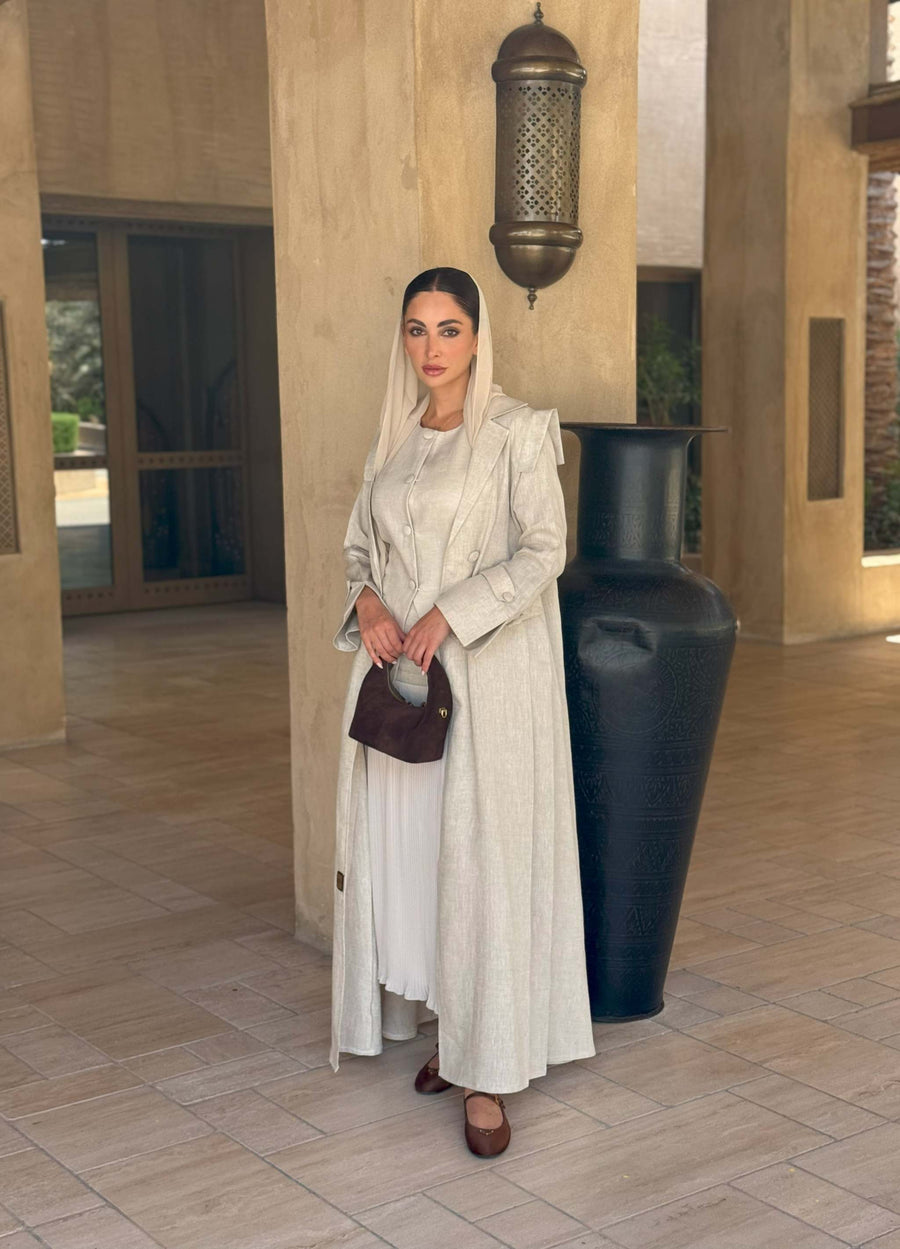 woman wearing a beige linen abaya with trench-style silhouette and matching sheila holding a brown handbag - beige abaya