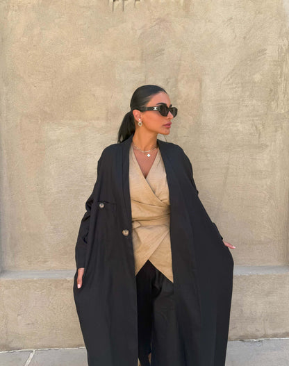 Woman wearing minimalist black linen abaya with straight cut and open front over beige outfit