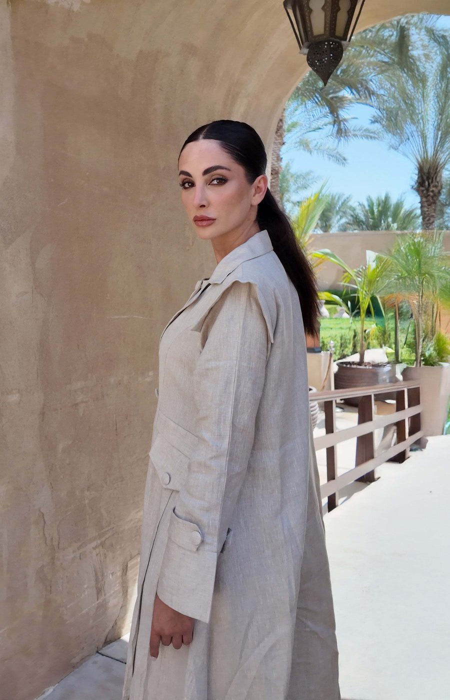 woman wearing a beige linen abaya with trench-style silhouette and matching sheila holding a brown handbag - beige abaya