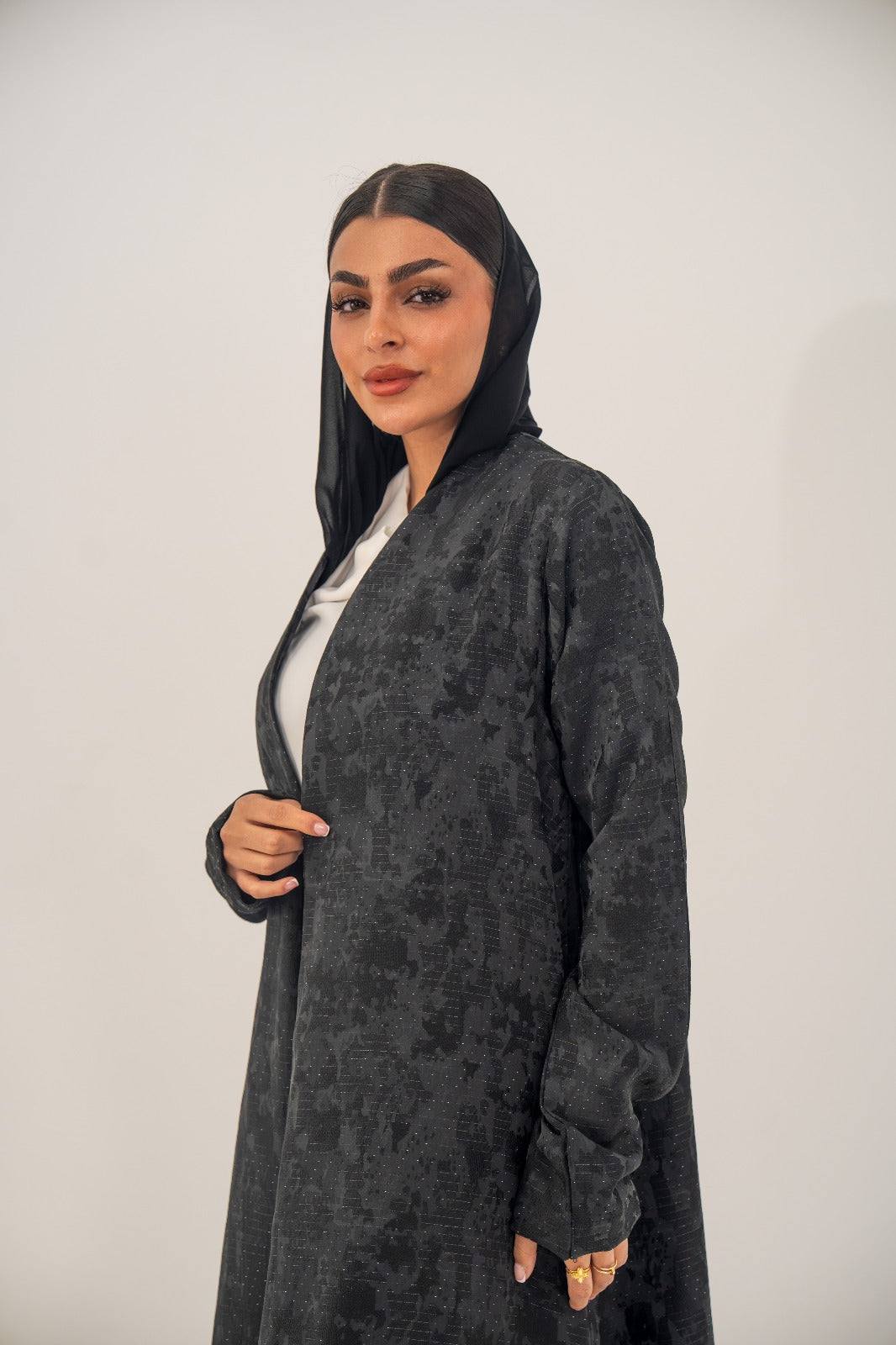Woman wearing an open-front black silk abaya with subtle abstract pattern and light shimmer in charcoal gray finish