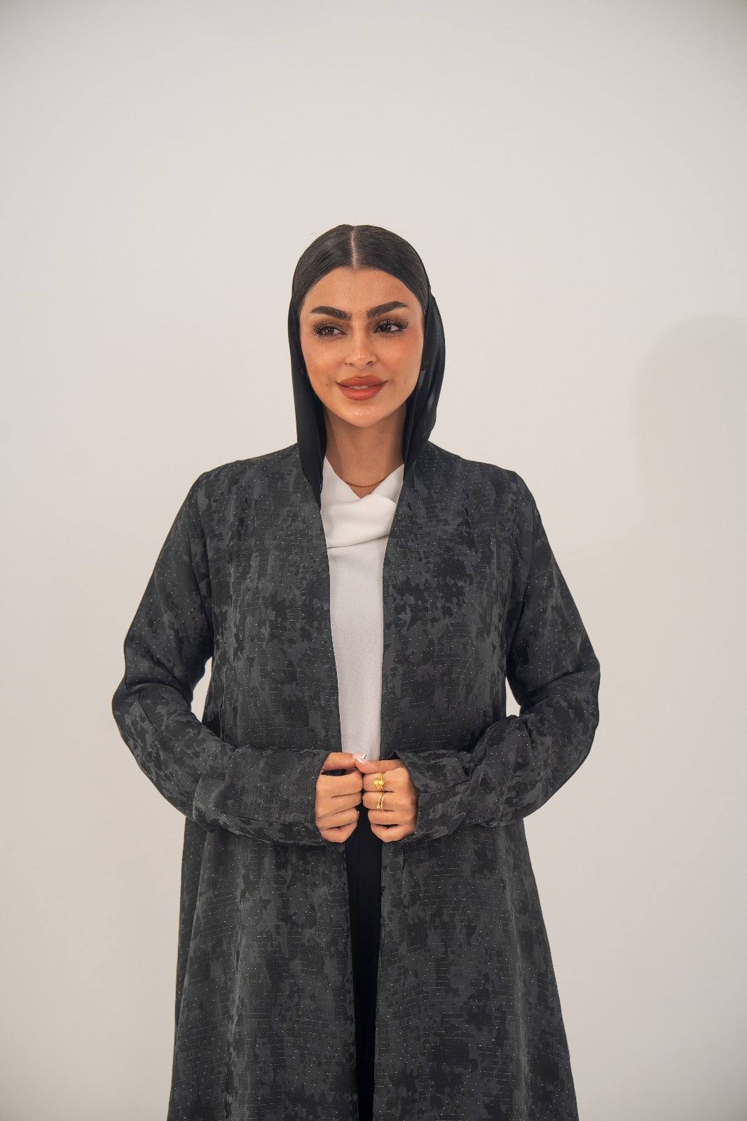 Woman wearing charcoal gray open-front abaya with subtle woven abstract pattern and light shimmer over white outfit