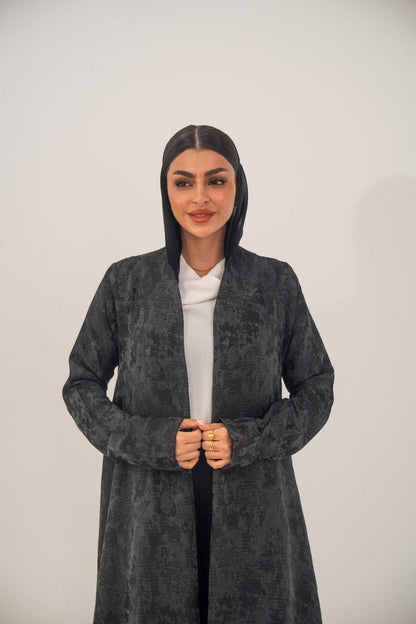Woman wearing charcoal gray open-front abaya with subtle woven abstract pattern and light shimmer over white outfit