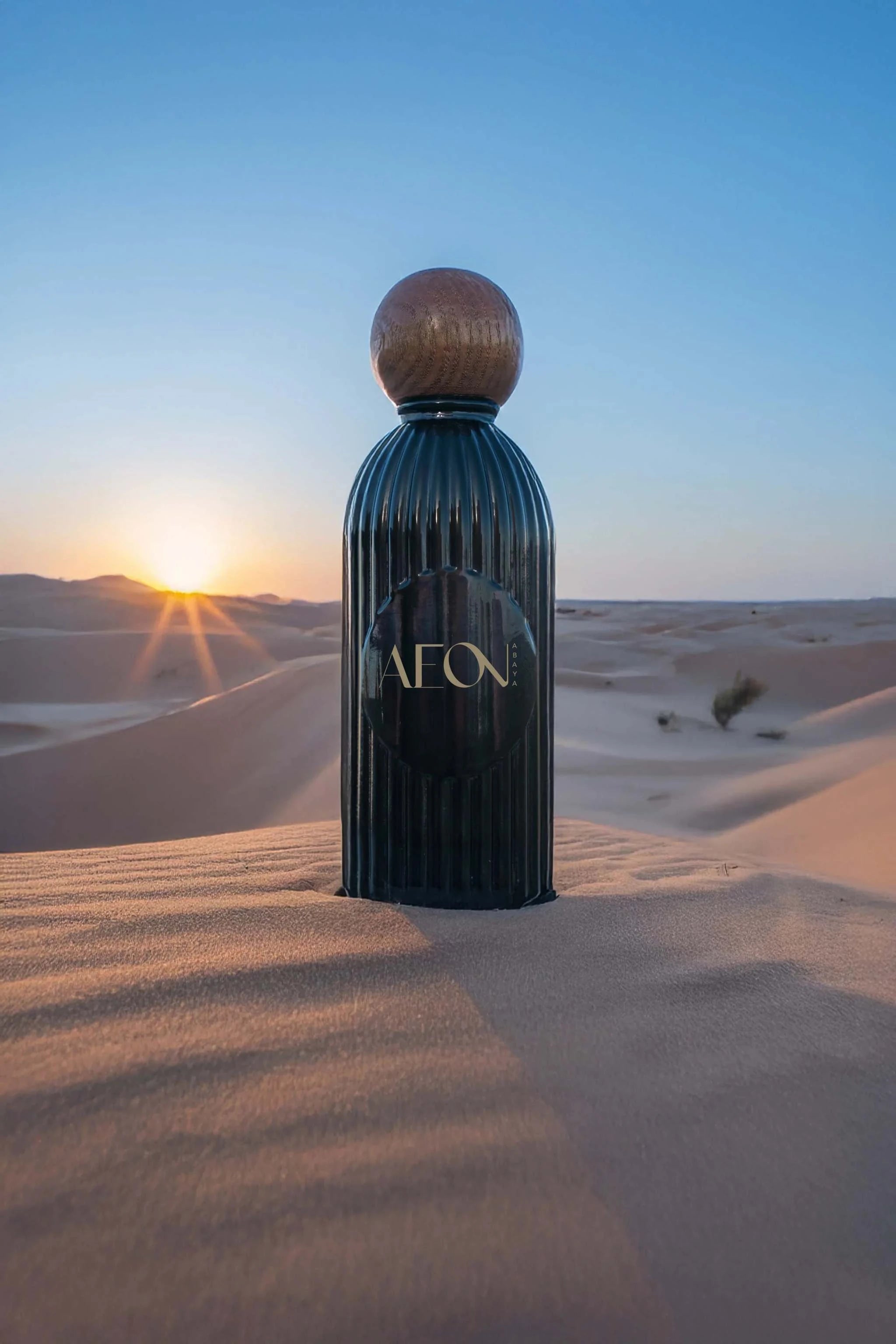 Aeon Scents elegant black fragrance bottle with wooden cap in desert at sunrise